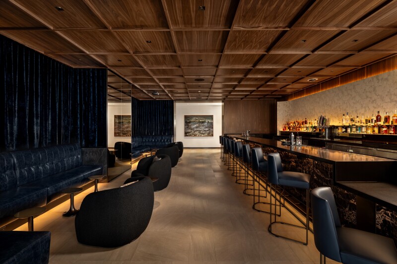 One of two bar areas in the United Polaris lounge at O'Hare is a speakeasy-style space with low lighting, a row of leather bar stools along the long bar, and club seating and navy blue leather banquettes along the other wall