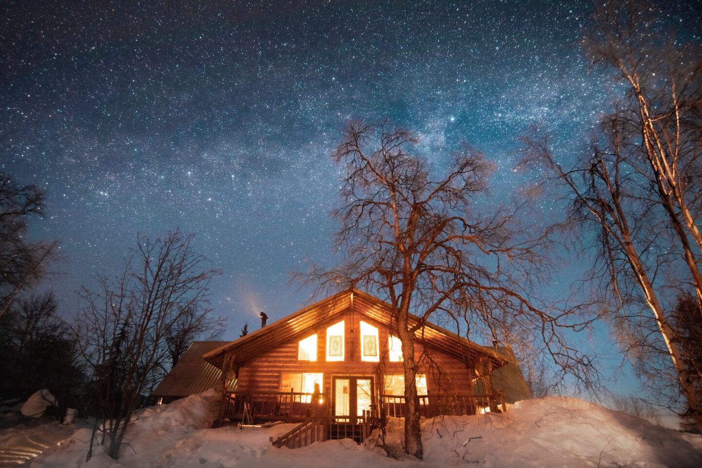 Exterior of lit-up Winterlake Lodge at night, with a few bare trees nearby